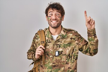 Hispanic young man wearing camouflage army uniform pointing finger up with successful idea. exited and happy. number one.