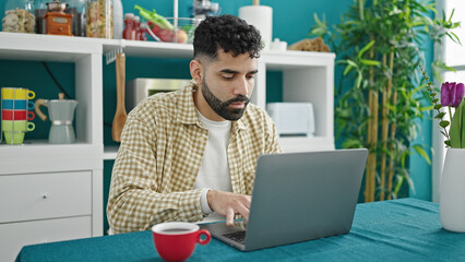 Young hispanic man using laptop sitting on table at dinning room