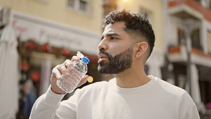 Young hispanic man drinking water at street