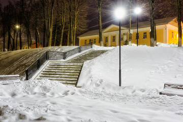 Winter city landscape in the light of street lighting. View from the snow-covered stairs from embankment to the administration of Torzhok.