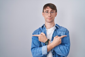 Caucasian blond man standing wearing glasses pointing to both sides with fingers, different direction disagree