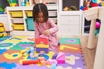 African american girl playing with wooden construction blocks sitting on floor at kindergarten