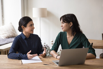 Serious Indian mentor or teacher talk to female colleague teach intern, discussing new project or...