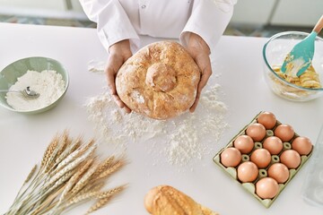 Young woman wearing cook uniform holding bread at kitchen