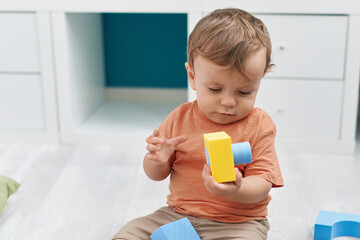 Adorable blond toddler playing with geometry blocks sitting on floor at kindergarten