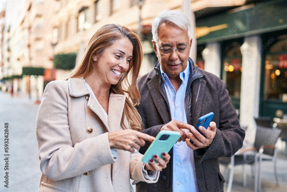 Wall mural Middle age man and woman couple smiling confident using smartphone at street