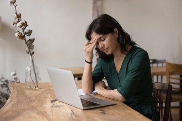 Overworked woman feels tired, looks concerned about on-line problem solution at workplace, frustrated by business bankruptcy, got bad news, suffers from migraine, experiences emotional stress at work