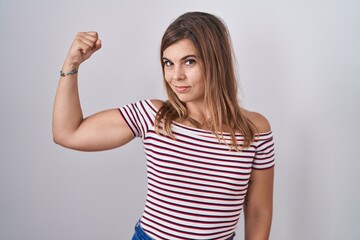 Young hispanic woman standing over isolated background strong person showing arm muscle, confident...