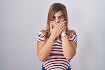 Young hispanic woman standing over isolated background shocked covering mouth with hands for...