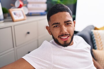 Fototapeta premium Young latin man smiling confident sitting on sofa at home