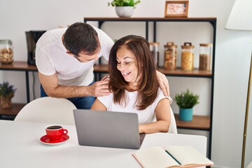 Middle age man and woman couple hugging each other working sitting on table at home