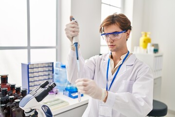 Fototapeta premium Young caucasian man scientist pouring liquid on test tube at laboratory