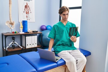 Young caucasian man physiotherapist looking xray using laptop at rehab clinic