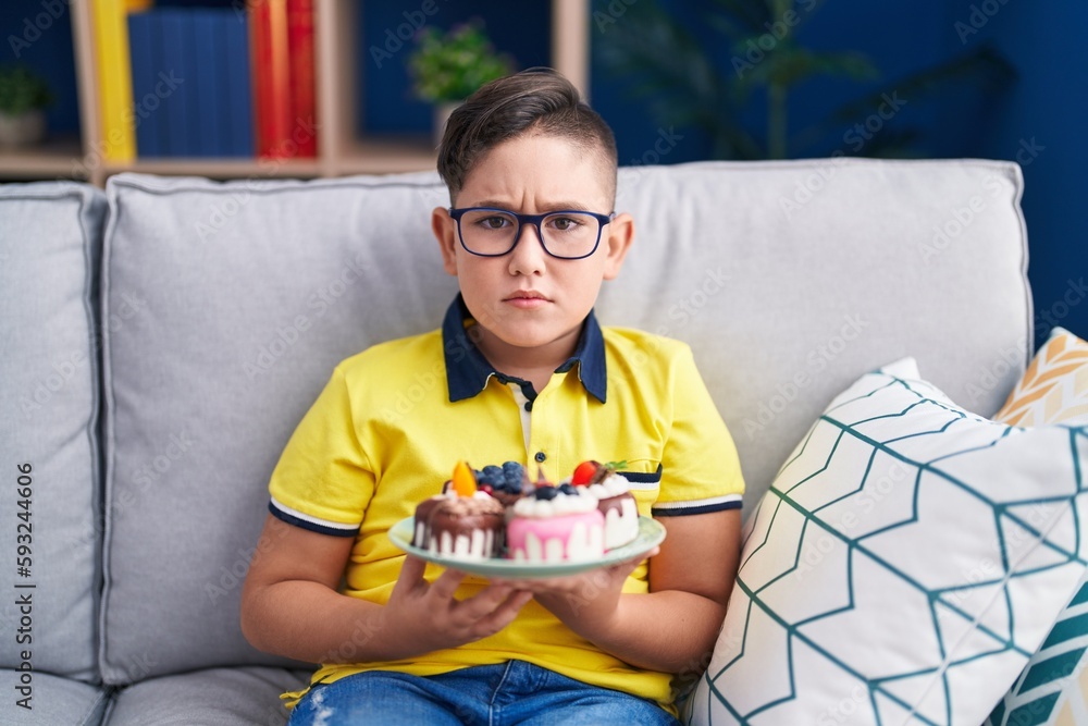 Poster Young hispanic kid holding cake sweets skeptic and nervous, frowning upset because of problem. negative person.