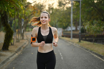 Delighted athletic woman in sportswear jogging in public park. Healthy lifestyle, sport, wellness concept