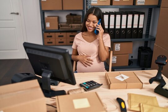 Young latin woman pregnant business worker talking on the smartphone at office