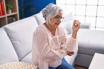 Middle age grey-haired woman sitting on sofa suffering for elbow pain at home