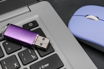 Modern laptop, purple USB flash drive and blue mouse on black grunge background
