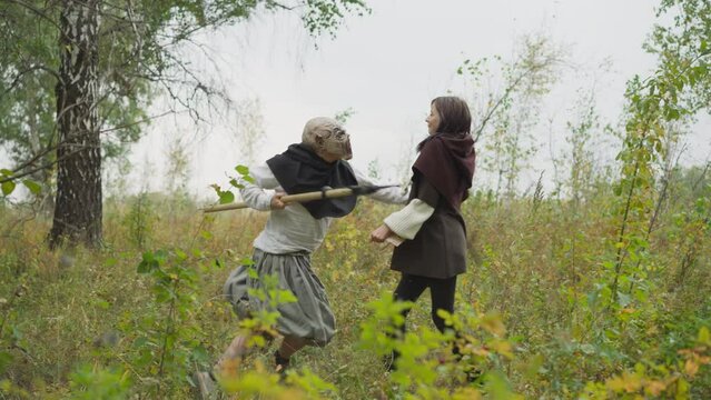 Goblin with ax runs between trees and attacks girl with spear. Female warrior fights monster. Duel between young lady and evil creature horizon tilts