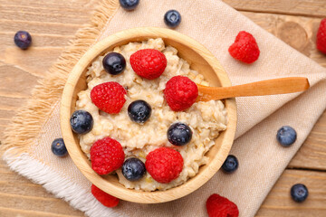 Bowl with tasty oatmeal, blueberries and raspberries on wooden background