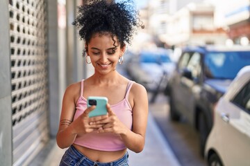 Young hispanic woman smiling confident using smartphone at street