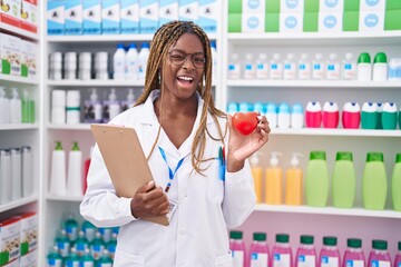 African american woman with braided hair working at pharmacy drugstore winking looking at the...