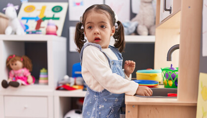 Adorable hispanic girl playing with play kitchen standing at kindergarten