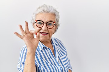 Senior woman with grey hair standing over white background smiling positive doing ok sign with hand and fingers. successful expression.