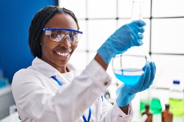 African american woman wearing scientist uniform measuring liquid laboratory