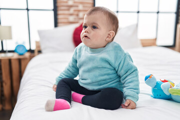 Adorable hispanic baby sitting on bed with relaxed expression at bedroom