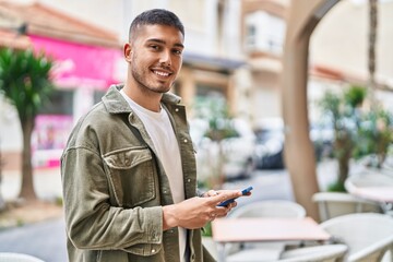 Young hispanic man smiling confident using smartphone at street