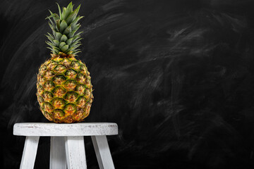 Pineapple fruit on a chair with blackboard background copy space for text.