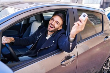 Young hispanic man smiling confident holding key of new car at street
