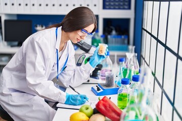 Young beautiful hispanic woman scientist holding macaroni writing on document at laboratory