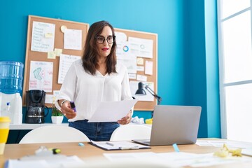 Young beautiful hispanic woman business worker standing by desk speaking at office