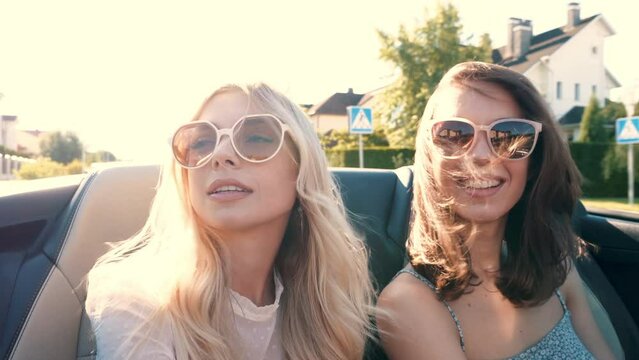 Portrait of two young beautiful and smiling hipster female in convertible car. Sexy carefree women driving. Positive models riding and having fun outdoors. Enjoying summer days. Cheerful and happy