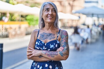 Middle age grey-haired woman standing with arms crossed gesture at street