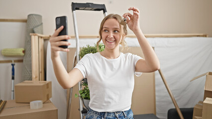 Young blonde woman having video call holding key at new home