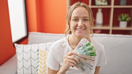 Young blonde woman smiling confident holding russia rubles banknotes at home