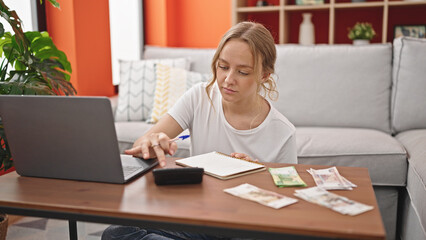 Young blonde woman using calculator counting ruble banknotes at home