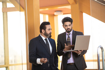 Young Indian manager showing project detail in laptop and discussing with his boss or senior.