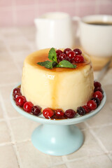 Dessert stand with delicious pudding, mint and cranberries covered by caramel syrup on tile background