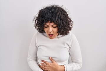 Hispanic woman with curly hair standing over isolated background with hand on stomach because...
