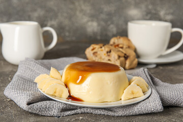 Plate with delicious pudding and bananas covered by caramel syrup on grey grunge background