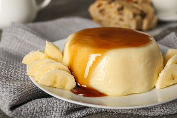 Plate with delicious pudding and bananas covered by caramel syrup on grey napkin, closeup