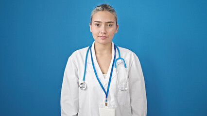 Young beautiful hispanic woman doctor standing with serious expression over isolated blue background