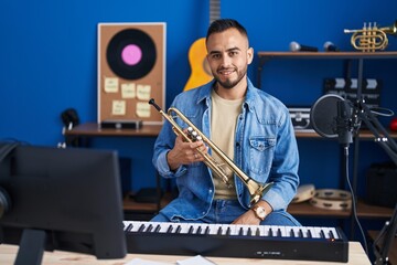 Young hispanic man musician smiling confident holding trumpet at music studio