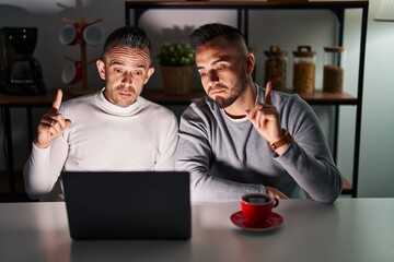 Homosexual couple using computer laptop pointing up looking sad and upset, indicating direction...