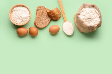 Composition with wheat flour, bread, eggs and wooden spoon on green background