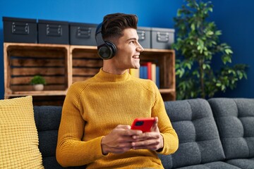 Young hispanic man listening to music sitting on sofa at home
